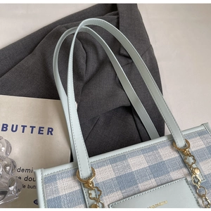 Detail of light blue checkered tote bag with gold flower chain on white desktop