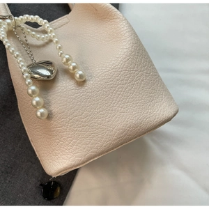 Vue détaillée du sac à main crème avec lanière en perles et pendentif cœur argenté