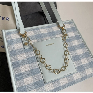 Detail of blue plaid tote bag with flower chain and brand logo on leather pocket