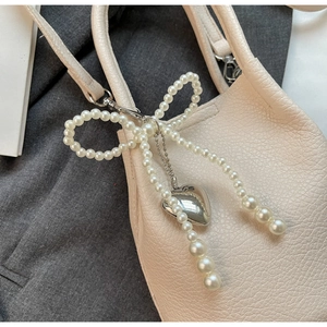 Détail de breloque nœud en perles avec pendentif cœur argenté sur sac à main en cuir