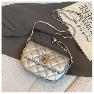 Close-up of silver quilted saddle bag with metal clasp and chain strap on newspaper