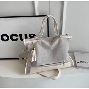 Macro detail of canvas tote with leather trim, golden hardware, and tassel accent
