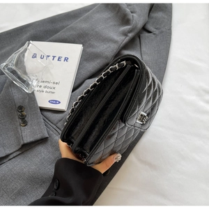 Detail of black quilted crossbody bag with silver turn-lock and leather chain strap