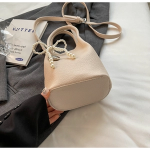 Vue détaillée du sac seau en cuir crème avec noud en perles et pendentif coeur argent