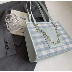 Close-up of light blue checkered tote bag with gold floral chain and leather handles