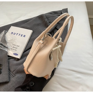 Détail du sac beige à motif litchi avec nœud en perles et breloque cœur sur veste