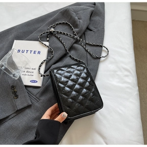 Detail of a black quilted chain bag styled over a grey blazer for a modern aesthetic look