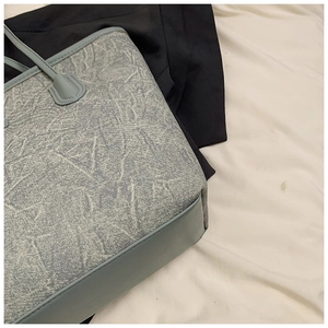 Close-up of light blue denim texture tote bag with leather straps and mixed materials