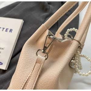 Détail d'un sac à main beige en cuir avec des clips argentés et un ornement perlé