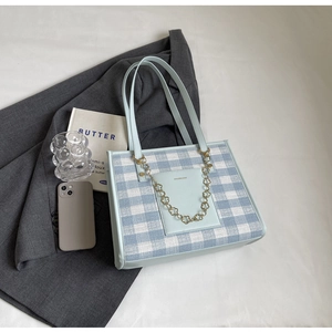 Detail of blue plaid tote bag with golden flower chain and leather pocket on blazer