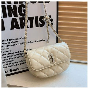 Detail of beige quilted saddle bag featuring a silver ball pendant and metal chain strap