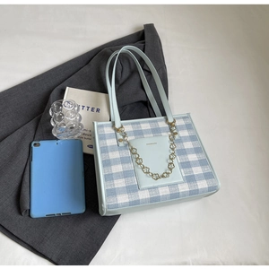 Detail of blue plaid tote bag featuring leather pocket and gold floral chain accessory