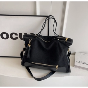 Detail view of large black canvas tote bag with gold hardware and leather tassels