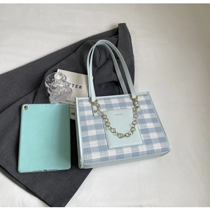 Detail view of a blue plaid tote bag with leather handles and a golden flower chain charm