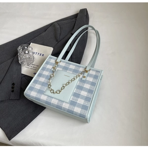 Close-up of light blue plaid tote bag with golden flower chain on white background