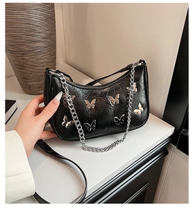 Detail of black pleated shoulder bag with silver 3D butterfly charms and chain strap
