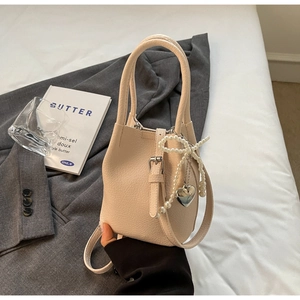 Détail du sac seau en cuir crème avec chaîne en perles et pendentif cœur dans un décor chic