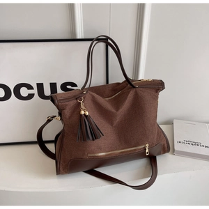 Detail of canvas tote bag with brown leather trim, golden zipper, and tassel charm