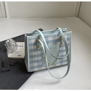 Detail of light blue plaid fabric and leather pocket on a modern tote bag with gold chain