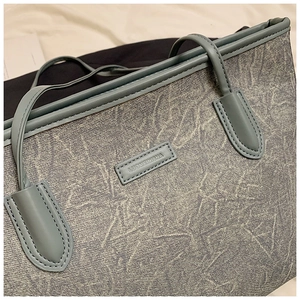 Detail of grey-blue textured tote bag featuring brand tag and reinforced stitching