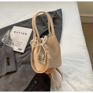 Détail du sac seau beige grainé avec nœud en perles et pendentif cœur en argent