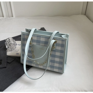 Detail of blue plaid tote bag featuring a golden flower chain and leather front pocket