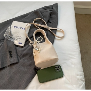 Détail du sac seau blanc cassé avec texture litchi et breloque nœud perlé et cœur argenté