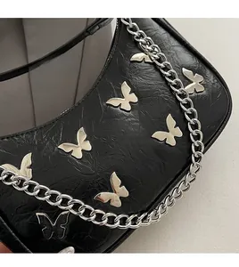 Detail of black wrinkled patent leather bag with silver butterfly charms and chunky chain