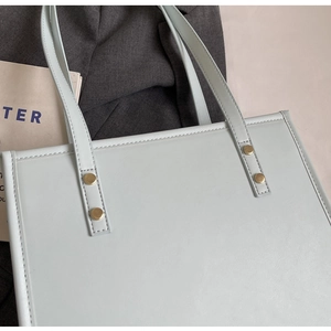 Detail of light blue leather tote bag with gold metal rivets and shoulder strap