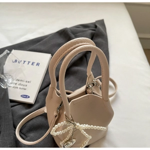Détail du mini sac cabas crème en cuir avec nœud en perles et pendentif cœur argenté
