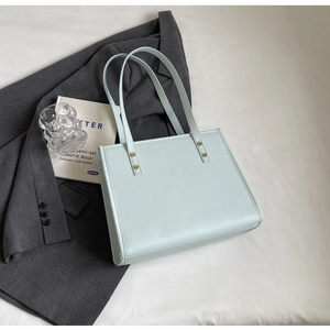 Detail of light blue faux leather tote bag with gold rivets and slim shoulder straps