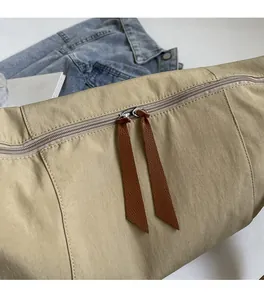 Detailed macro view of smooth dual metal zippers with brown leather pullers on beige canvas bag