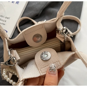 Gros plan du sac crème avec poignée en perles, texture grainée et double fermoir magnétique