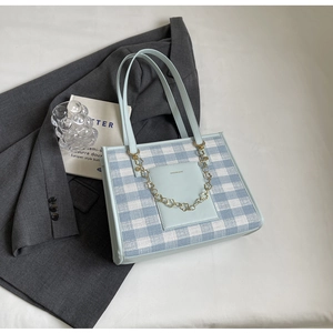 Detail of light blue plaid tote bag featuring golden floral chain and front pocket