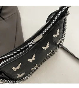 Detail of a smooth silver zipper and butterfly metal charms on a black pleated bag