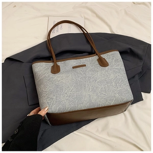 Detail of grey denim tote bag with brown leather accents and spacious interior design