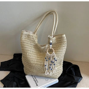 Macro detail of beige woven straw tote bag featuring a blue evil eye tassel charm