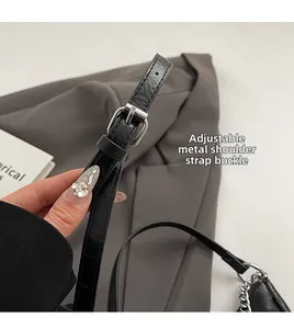 Detail of adjustable black crocodile pattern strap with silver metal buckle on bag
