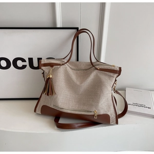 Detail of canvas tote bag with brown leather trim, tassel charm and gold hardware