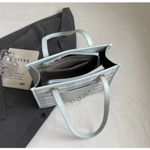 Detail of blue striped woven tote bag featuring leather trim and floral chain accessory