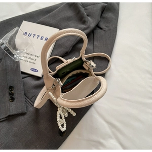 Gros plan sur le mini sac fourre-tout en cuir crème avec breloque perle sur un blazer