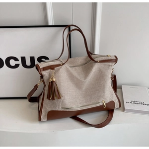 Detail view of large canvas tote bag with brown leather trim and tassel on a desk