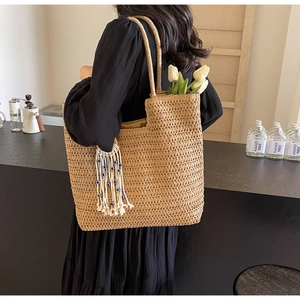 Detail of straw woven tote bag featuring evil eye bead tassel and long shoulder strap