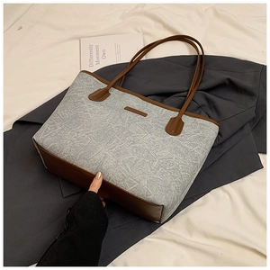 Detail of grey-blue textured tote bag with dark brown leather handles on grey suit