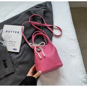 Détail du sac seau en cuir rose avec breloque nœud en perles et pendentif cœur argenté