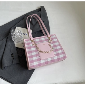 Macro detail of pink checkered tote bag featuring gold chain and textured fabric surface