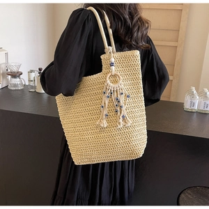 Detail of woven straw tote bag featuring white tassel with blue evil eye bead accent