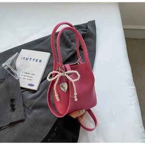 Détail du sac seau rose en cuir grainé avec nœud en perles et pendentif cœur