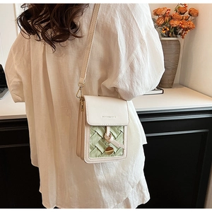 Detail of crossbody phone bag in beige leather with a green woven panel and gold charm