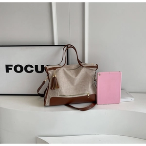 Detail of beige canvas tote bag with brown leather trim and tassel on a white platform